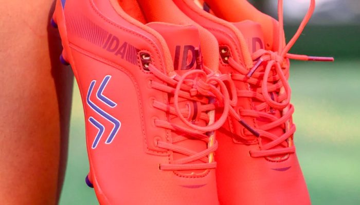 Photograph of woman footballer holding IDA Sports football boots in bright orange colour