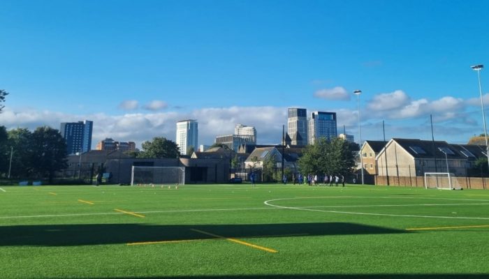 Photograph of the Cardiff Bay women's football hub venue, which is a 3G pitch with Cardiff City Centre in the background